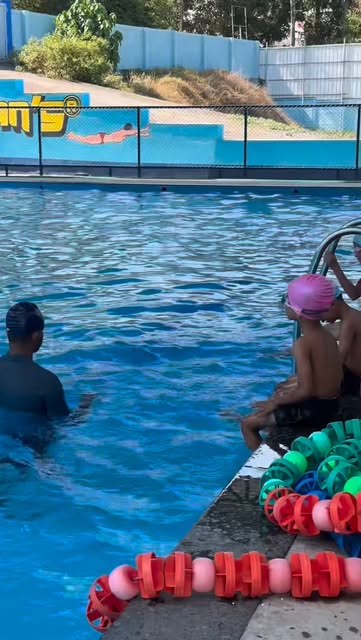Kids learning to swim with a coach by the lane ropes